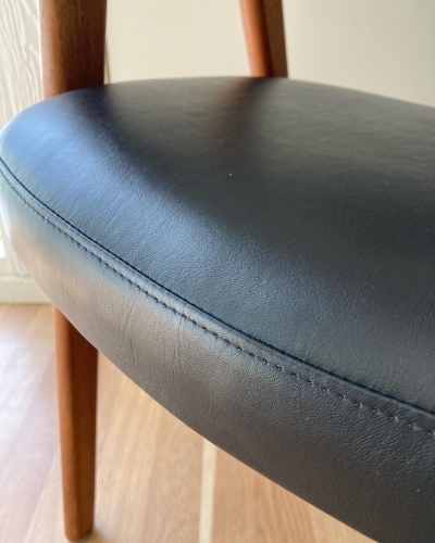 Close up af teak stol med sort læder ombetrækning.